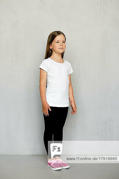 Niedliches kleines Kind mit langen Haaren in weißem T-Shirt und schwarzer Jogginghose posiert