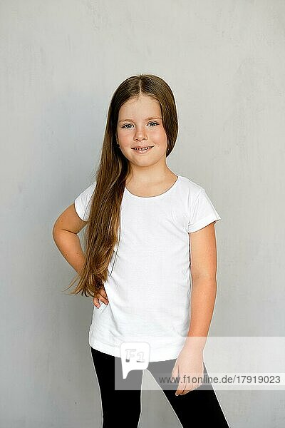 Cute young child with long hair in white t-shirt and black sweatpants posing
