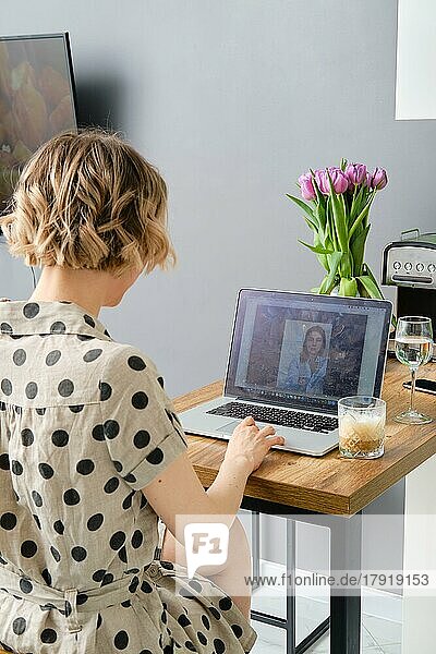Rückansicht einer Frau  die mit ihrem Laptop einen Videoanruf bei einem Geschäftspartner tätigt und auf den Bildschirm mit einem virtuellen Web-Chat schaut