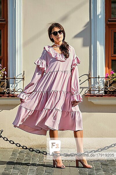 Outdoor urban portrait of young beautiful stylish girl in oversized pink dress