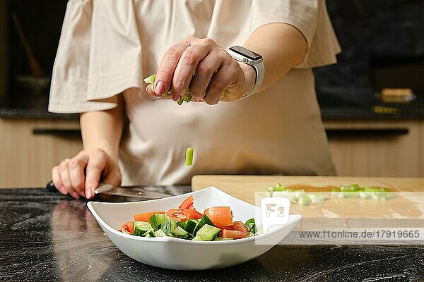 Nahaufnahme der Hand einer Frau  die eine geschnittene Selleriestange in einen Teller mit Salat fallen lässt