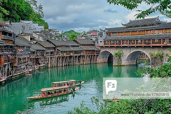 FENGHUANG  CHINA  23. APRIL 2018: Chinesische Touristenattraktion  Feng Huang Ancient Town (Phoenix Ancient Town) am Tuo Jiang Fluss mit Brücke und Touristenboot. Provinz Hunan  China  Asien
