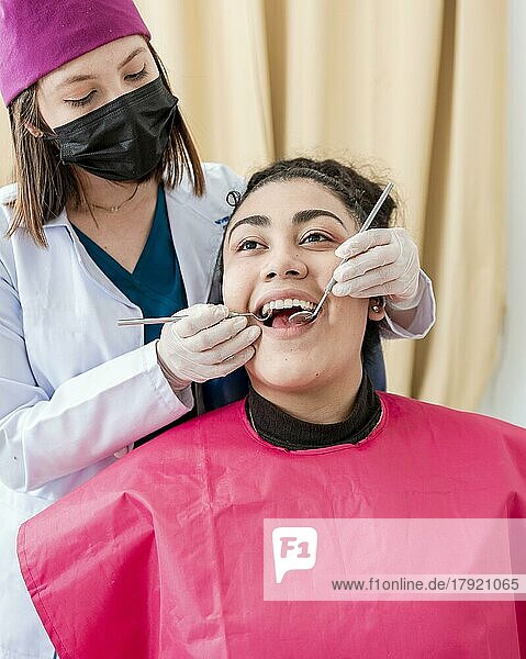 Zahnarzt kontrolliert Patient mit Bagger und Zahnspiegel  Frontansicht des Zahnarztes bei der Kontrolle des Patienten mit Bagger und Zahnspiegel  Patient vom Zahnarzt kontrolliert  Zahnarzt bei der Zahnkontrolle