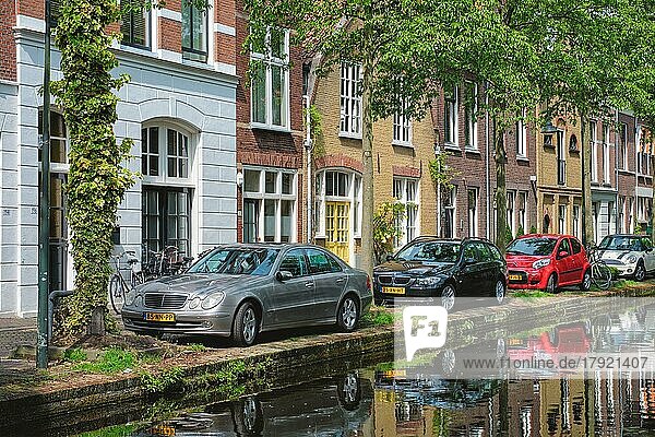 Autos und Fahrräder geparkt auf Kanalböschung in Straße von Delft mit Reflexion. Delft  Delft  Niederlande  Europa