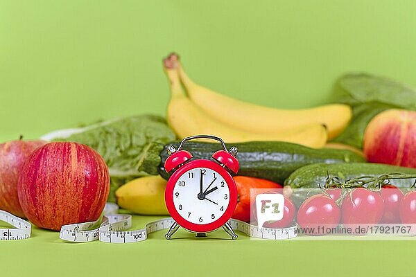 Diätkonzept zum Abnehmen  bei dem man sich nur zu bestimmten Zeiten gesund ernährt  mit Gemüse  Obst  Maßband und Uhr