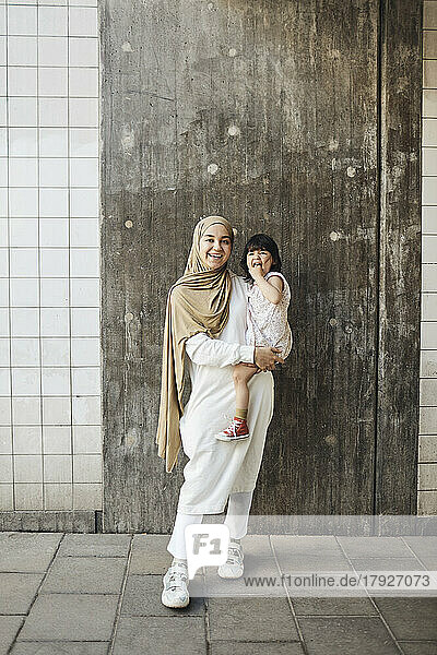 Porträt einer glücklichen Frau mit ihrer Tochter vor einer Wand stehend