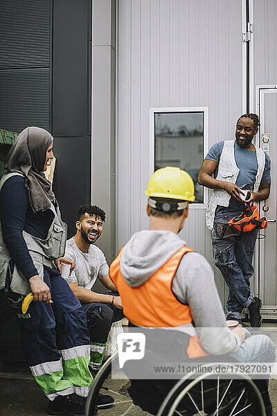 Happy young construction worker talking with male and female colleagues during break at site