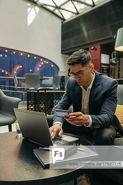 Male entrepreneur holding credit card while using laptop in hotel lounge