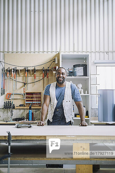 Portrait of smiling carpenter standing at workbench