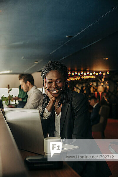 Smiling young businesswoman looking at laptop while sitting in hotel lounge