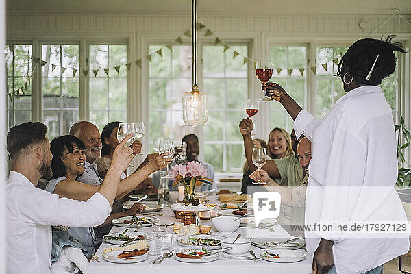 Frau stößt mit der Mehrgenerationenfamilie am Esstisch während einer Dinnerparty zu Hause an