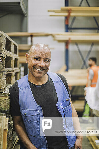 Glücklicher glatzköpfiger Zimmermann  der sich auf ein Holzregal im Lagerhaus stützt