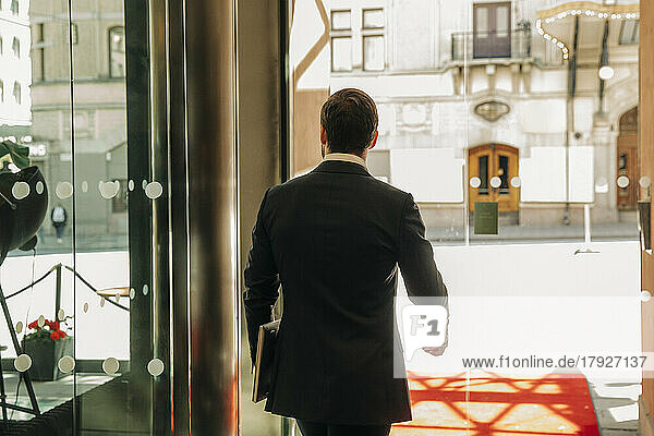 Rear view of young businessman with laptop leaving hotel