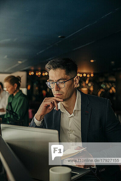Businessman with hand on chin looking at laptop while sitting in hotel