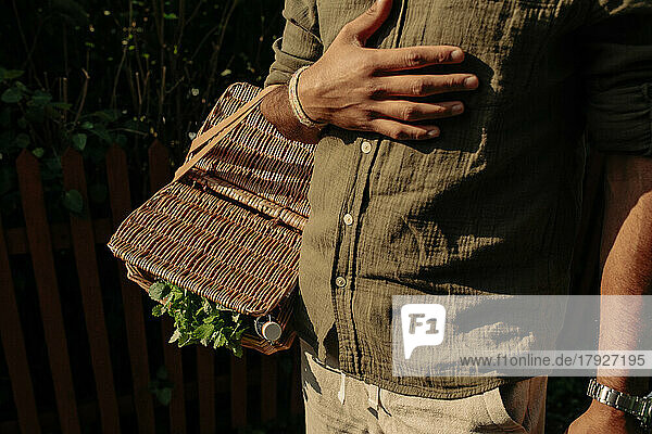 Midsection of man with hand on chest carrying picnic basket