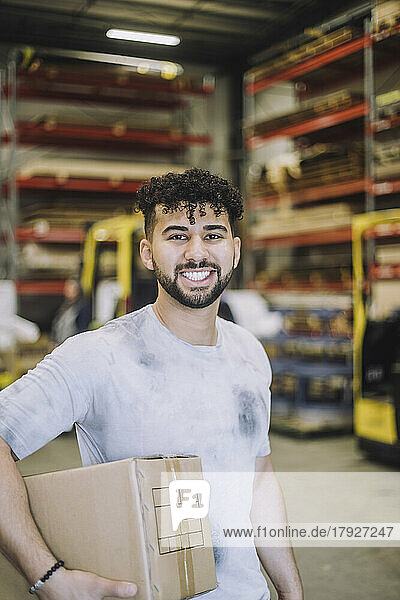 Porträt eines glücklichen jungen Zimmermanns mit Karton in einem Lagerhaus
