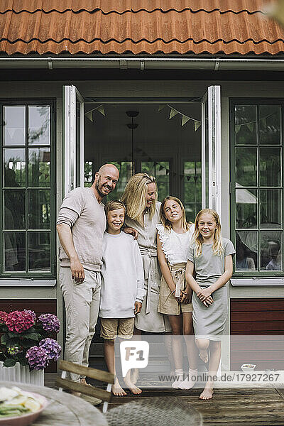 Portrait of happy family standing together against doorway on porch