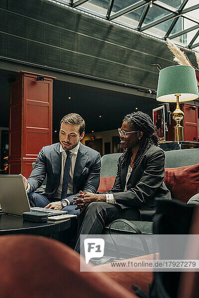 Männlicher Berufstätiger  der mit einer Kollegin über einen Laptop diskutiert  während er in einer Hotellounge sitzt