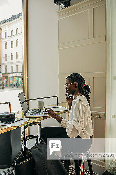 Seitenansicht eines weiblichen Berufstätigen  der am Schreibtisch im Büro sitzt und mit dem Handy telefoniert