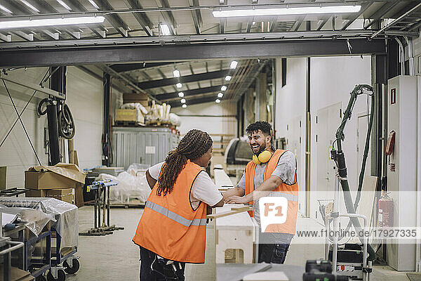 Female carpenter discussing with cheerful male colleague in warehouse