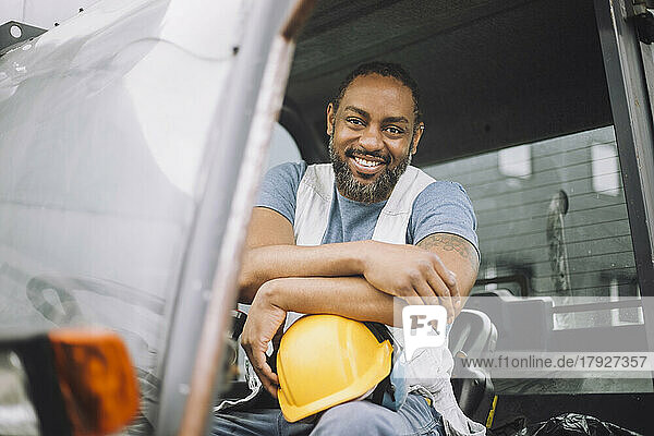 Porträt eines lächelnden reifen Bauarbeiters mit Schutzhelm  der in einem Fahrzeug sitzt