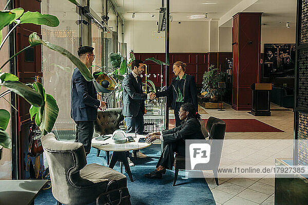 Mature businesswoman doing handshake with businessman by male and female colleagues in hotel lounge