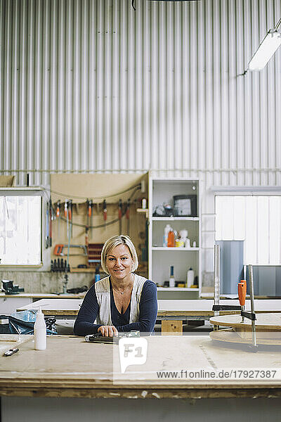 Portrait of smiling female carpenter leaning on workbench