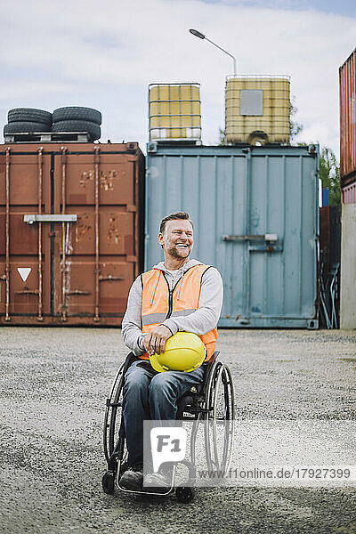 Full length of happy construction worker sitting in wheelchair at site