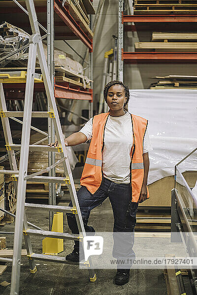 Confident female carpenter standing by ladder in warehouse