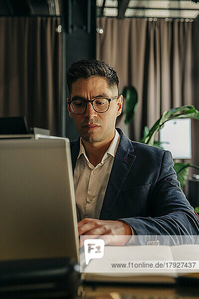 Mid adult businessman wearing eyeglasses using laptop while sitting in hotel lounge