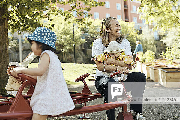 Happy father looking away while sitting and enjoying with daughter in kindergarten