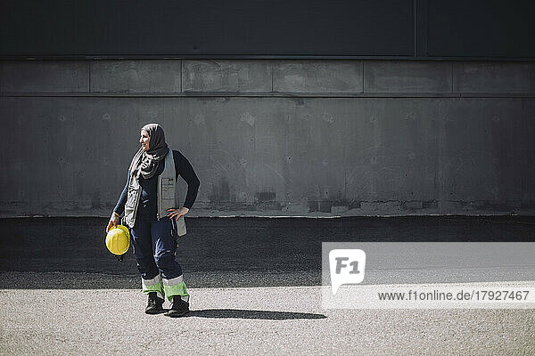 Bauarbeiterin in voller Länge mit Hand auf der Hüfte an der Straße stehend an einem sonnigen Tag