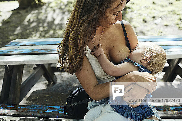 Mutter füttert ihre kleine Tochter mit Muttermilch  während sie auf einer Bank sitzt
