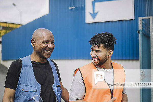 Glücklicher junger Bauarbeiter im Gespräch mit einem glatzköpfigen Kollegen auf der Baustelle