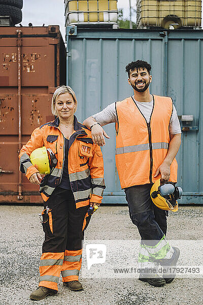 Full length of smile male and female construction workers in reflective clothing standing at site