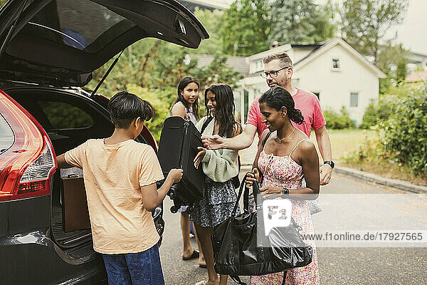 Multiracial family unloading luggage from car trunk while standing on road