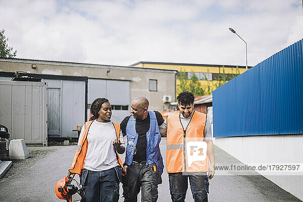 Weiblicher Bauarbeiter im Gespräch mit männlichen Kollegen beim Gehen auf der Straße