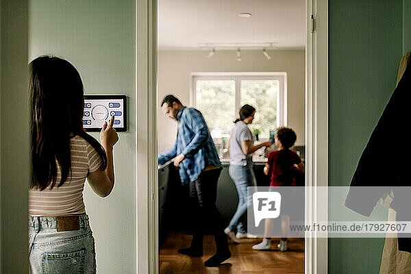 Rear view of girl using home automation on wall by doorway