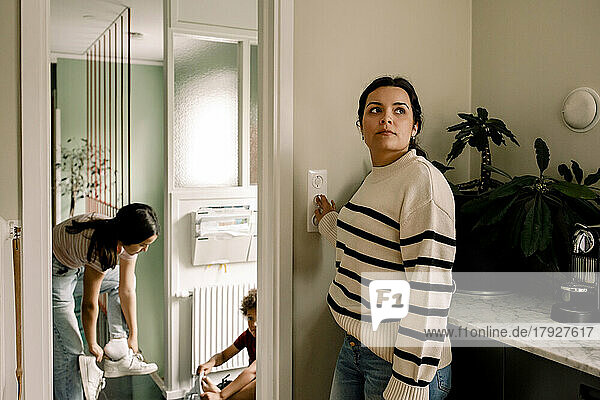 Frau  die den Lichtschalter ausschaltet  während sie zu Hause in der Nähe der Eingangstür steht