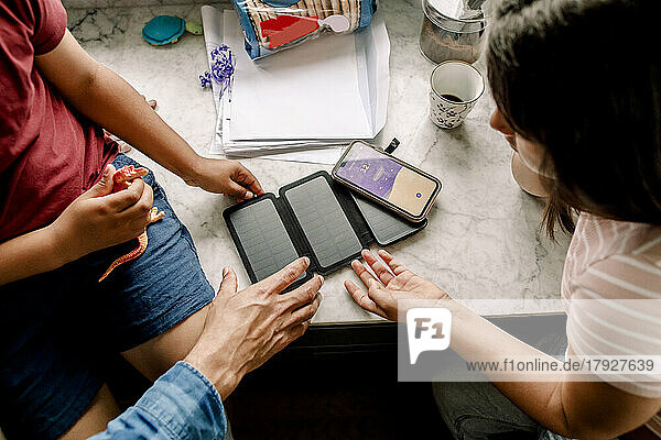 Blick von oben auf eine Familie mit Sonnenkollektor und Smartphone am Tisch