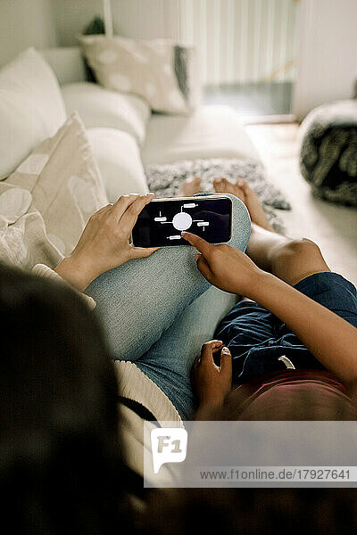 Mutter und Sohn nutzen die Hausautomatisierungs-App auf dem Smartphone  während sie auf dem Sofa liegen