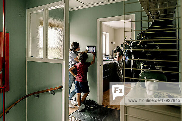 Junge  der mit seiner Mutter ein digitales Tablet benutzt  während er zu Hause in der Nähe der Tür steht