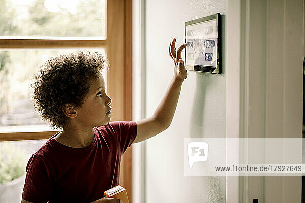 Junge mit lockigem Haar  der ein an der Wand montiertes Hausautomatisierungssystem benutzt