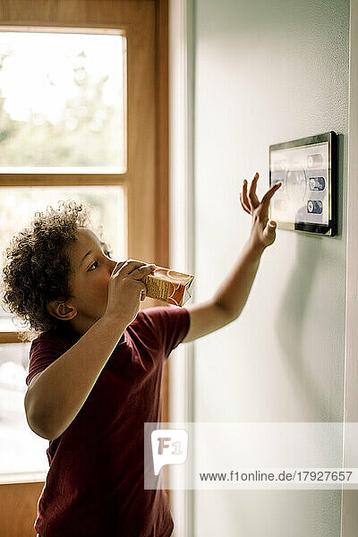 Junge nutzt die an der Wand montierte Heimautomatisierung und trinkt Saft