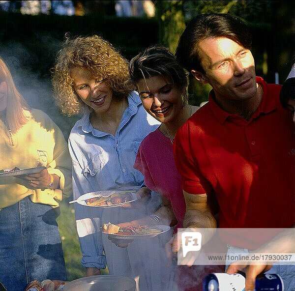 Gartenparty junge Leute beim Essen  Grillen  Grillparty  3 Personen  Frauen und Männer  Teller in der Hand  auf das Grillgut schauend