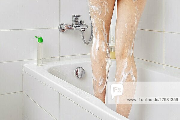 Ausgeschnittenes Foto einer Frau  die Duschgel benutzt  während sie im Badezimmer duscht und in der Badewanne steht. Nahaufnahme der schlanken weiblichen Beine mit Seifenlauge oder Schaum bedeckt. Hygiene und Körperwäsche Konzept