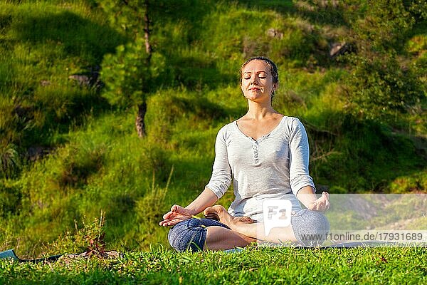 Junge sportliche Frau macht Yoga im Freien  meditiert und entspannt sich in Padmasana Lotus Pose) mit Kinn Mudra auf grünem Gras im Wald
