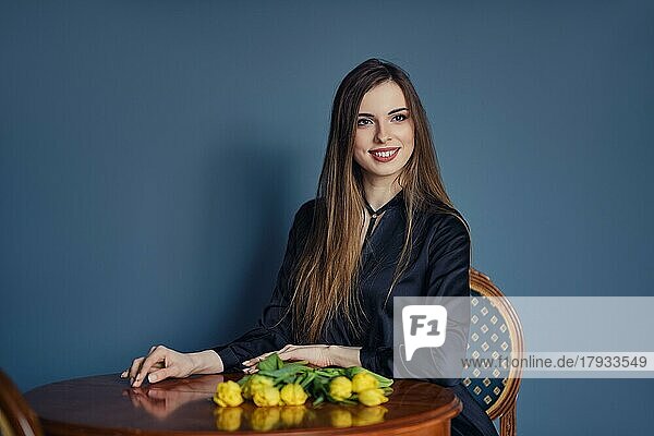 Schöne junge Frau sitzt hinter dem Tisch mit Tulpen