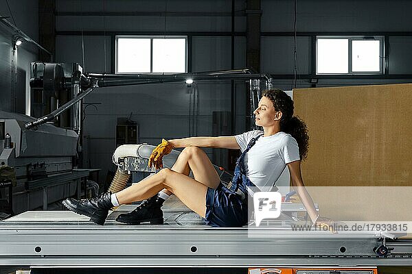 Junge Frau sitzt auf einer Schiene der Kreissäge einer Holzbearbeitungsmaschine