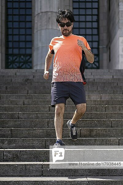 Porträt von gut aussehend attraktiv reifen bärtigen sportlichen lateinischen Mann Kerl 40s in orange T-Shirt läuft auf einigen Treppen